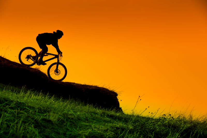 日落时下坡山地自行车骑行的轮廓