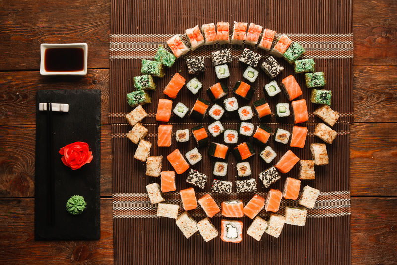 美食艺术，美味的寿司套装。各种各样的开胃面包卷，棕色草席上的彩色圆形装饰，平铺。豪华日本餐厅菜单照片。