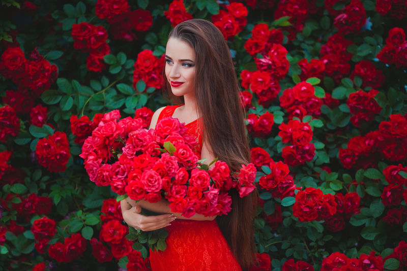 接近红玫瑰的性感黑发女郎的美丽画像
