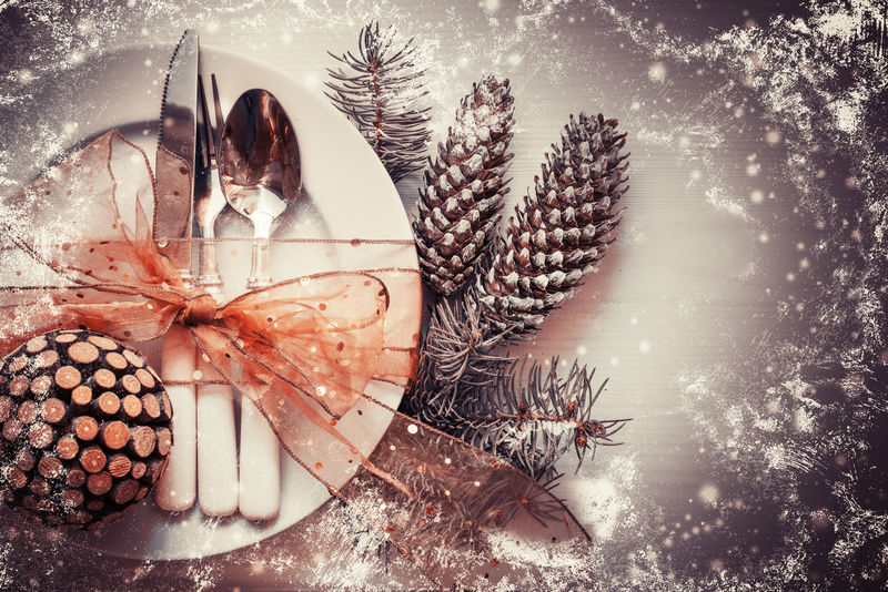 圣诞桌上摆放着圣诞松枝和盘子、母牛、叉子、丝带和蝴蝶结/圣诞假期背景