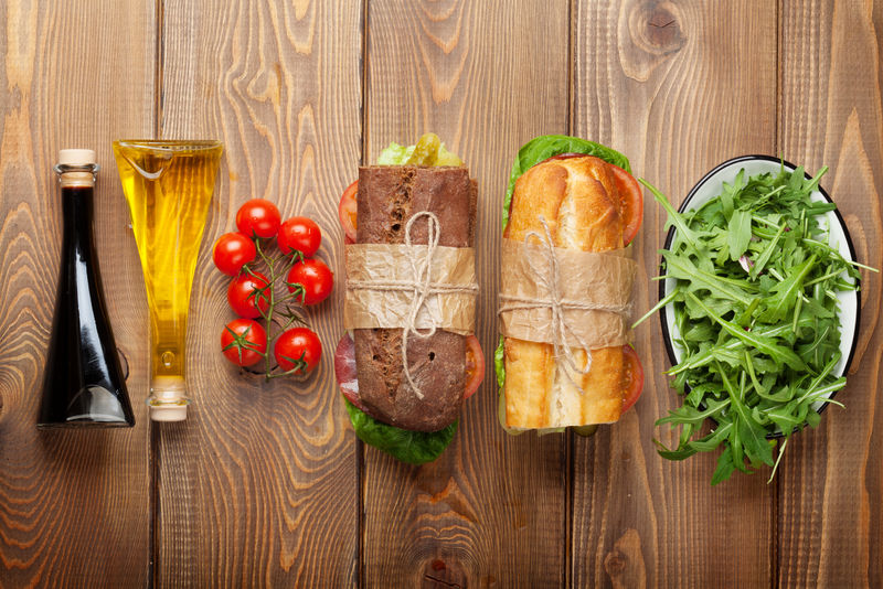 两个三明治-配沙拉、火腿、奶酪和西红柿-沙拉和香料放在木桌上-带复制空间的俯视图