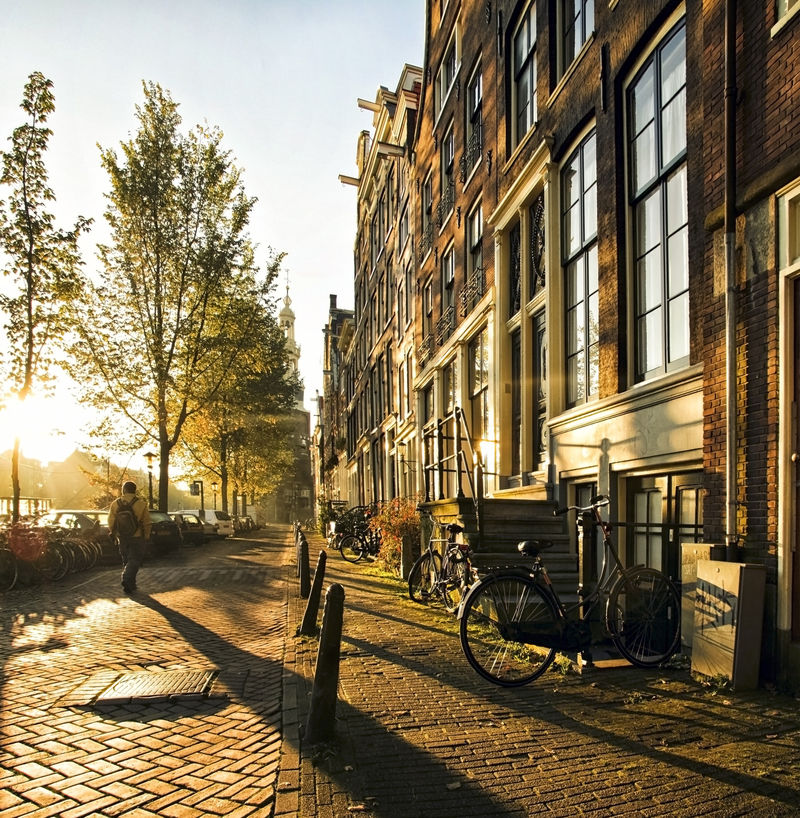 一个陌生人在阿姆斯特丹的街道上-伴随着长长的阴影-在这大气的日落中漫步在运河和住宅之间