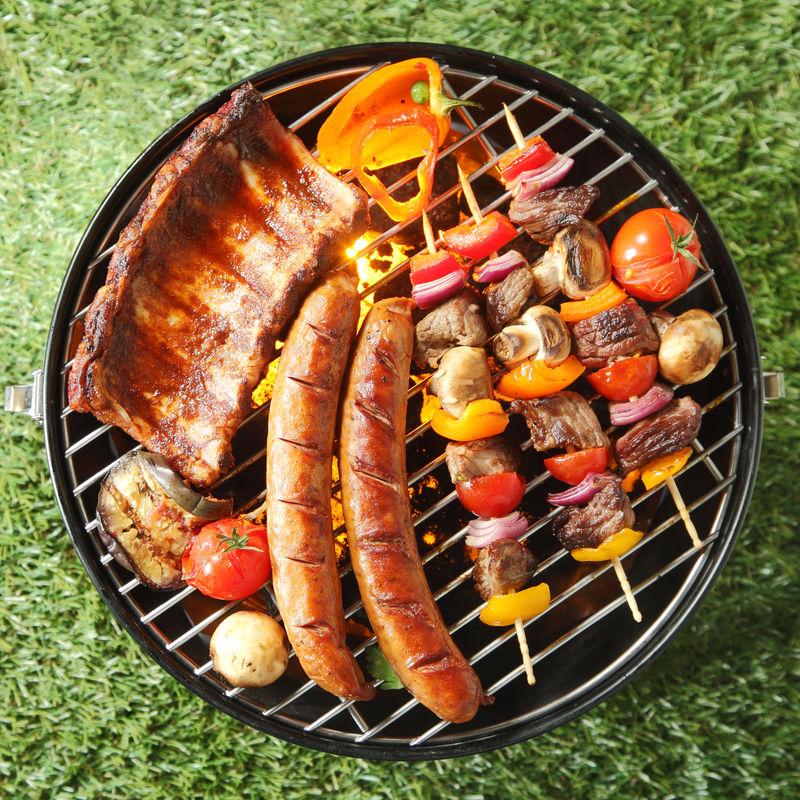 夏季烧烤时美味的各种肉类-包括香肠、牛肉串、番茄和蘑菇排骨-俯视绿草