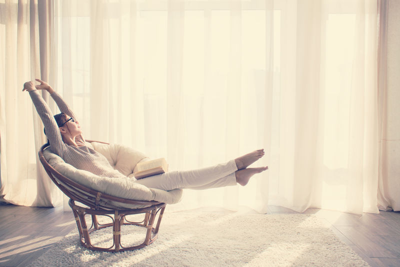 年轻的女人在家里坐在现代椅子在窗前她在客厅看书放松-Instagram调色