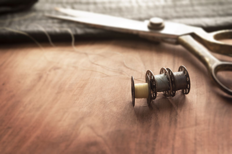 旧缝纫机的线轴用金（铜）剪刀和黑丝织物放在破旧的工作台上-裁剪工作台-纺织或细布制造