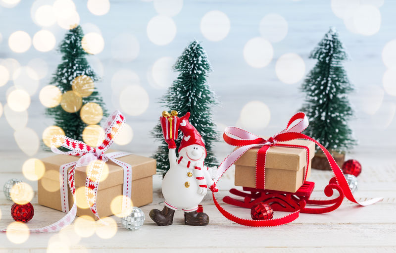 雪人、礼品盒和白色木质背景的装饰圣诞树