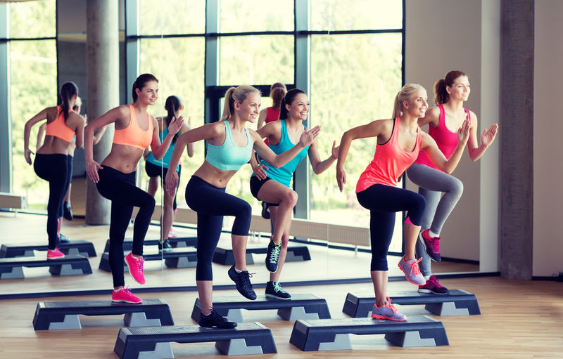 健身、运动、训练、健身房和生活方式概念-一群在健身房与步进者一起锻炼的女性