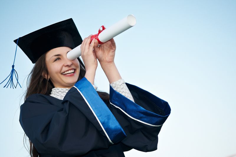 穿着长袍在户外看毕业证书的笑着的年轻女生