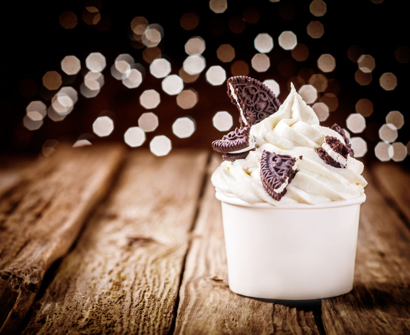 美味的派对甜点-冷冻酸奶和巧克力奥利奥-放在一个塑料外卖桶里-放在一个古老的木制柜台上-上面闪烁着节日的灯光