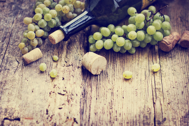 木桌上的一瓶白葡萄酒、葡萄和软木塞
