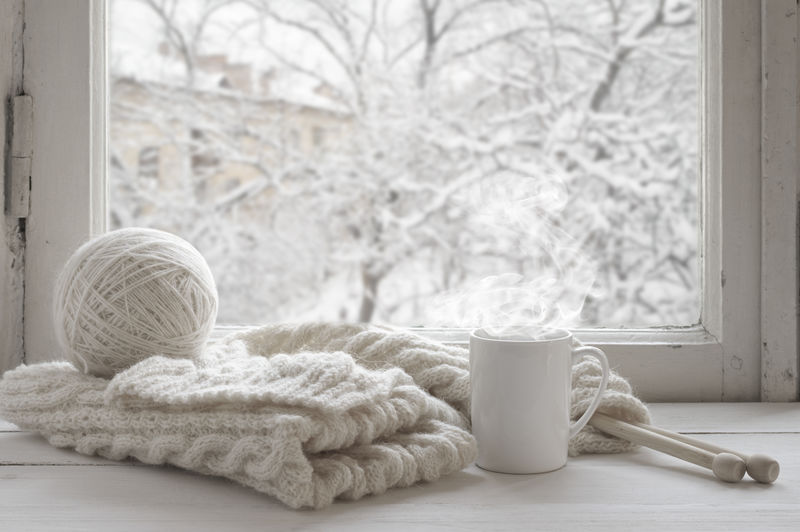 舒适的冬季静物生活：一杯热茶和温暖的羊毛编织在复古的窗台上-外面的雪景衬托着