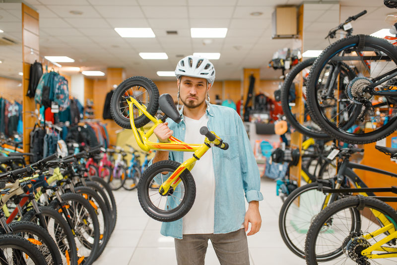 戴头盔的男子手持儿童自行车，运动商店
