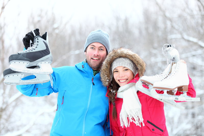 滑冰冬季情侣微笑着高兴和兴奋地在雪地里向户外展示溜冰鞋-美丽的年轻多种族夫妇健康的生活方式理念