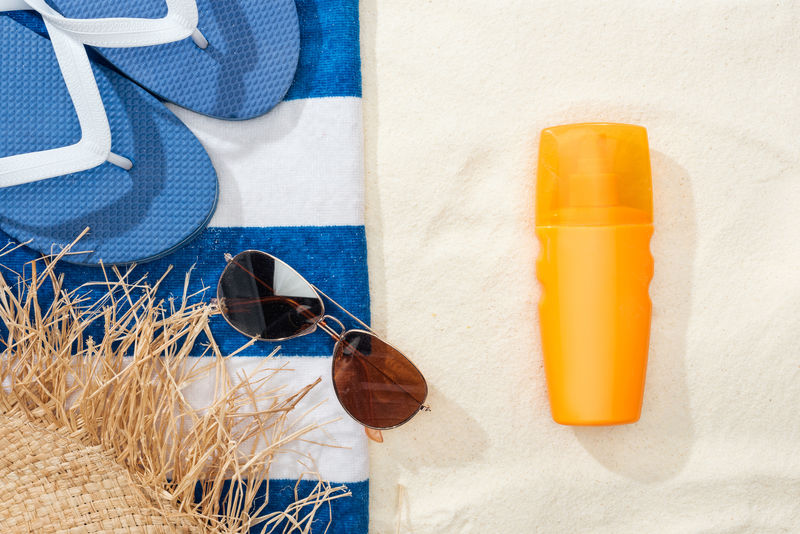 金色沙滩上的防晒霜、草帽、人字拖、太阳镜和蓝白条纹毛巾俯视图