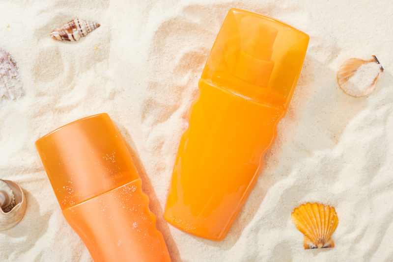 金沙滩上的橙色防晒霜瓶，带贝壳