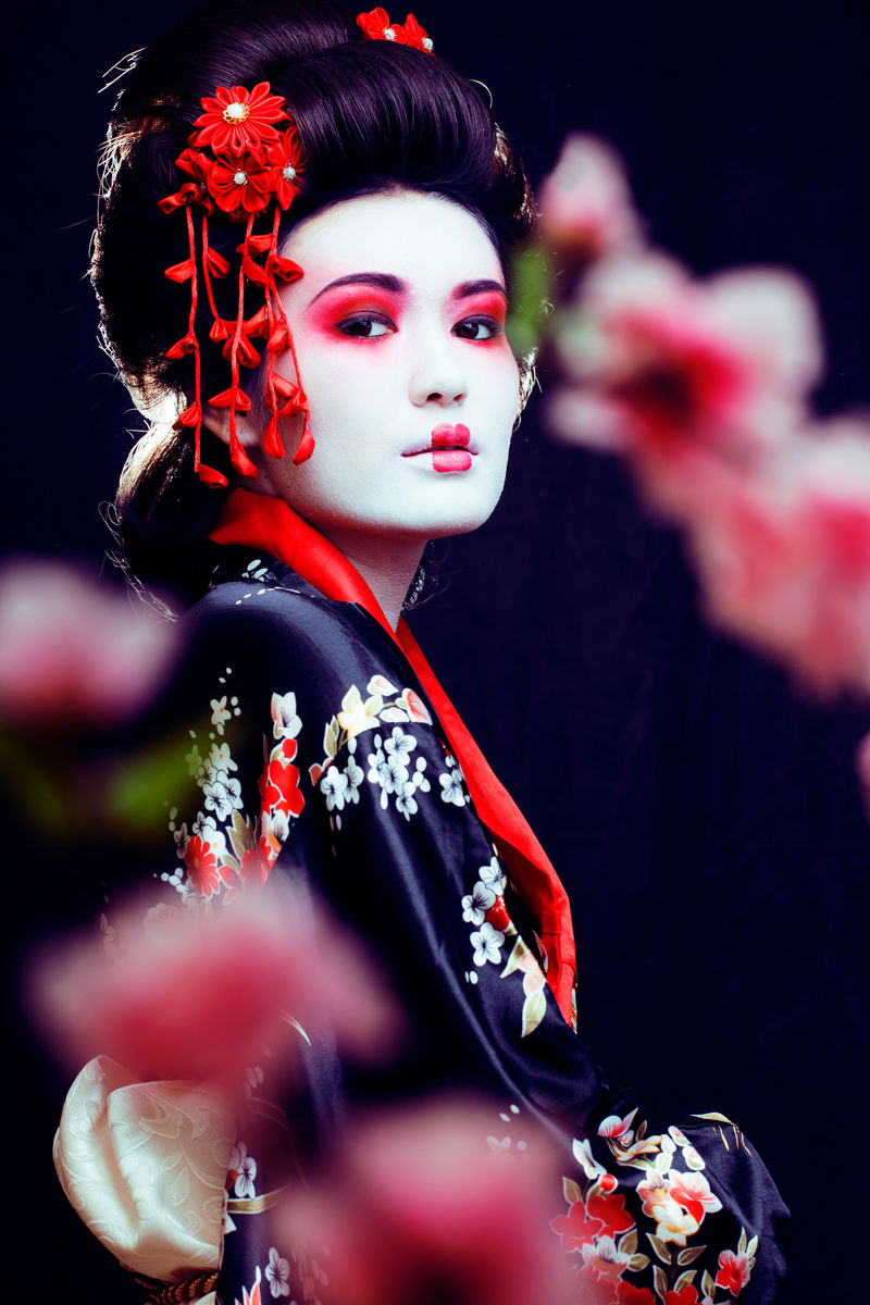 年轻漂亮的真正的艺妓，穿着和服，樱花，黑底装饰。