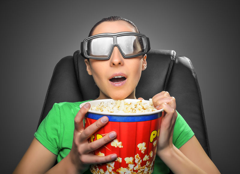 观看者用盛满爆米花碗的眼镜观看3D影院