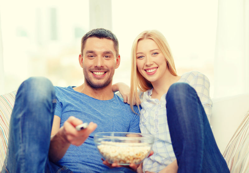 食物-爱情-家庭和幸福的概念-带着爆米花的微笑情侣在家看电影