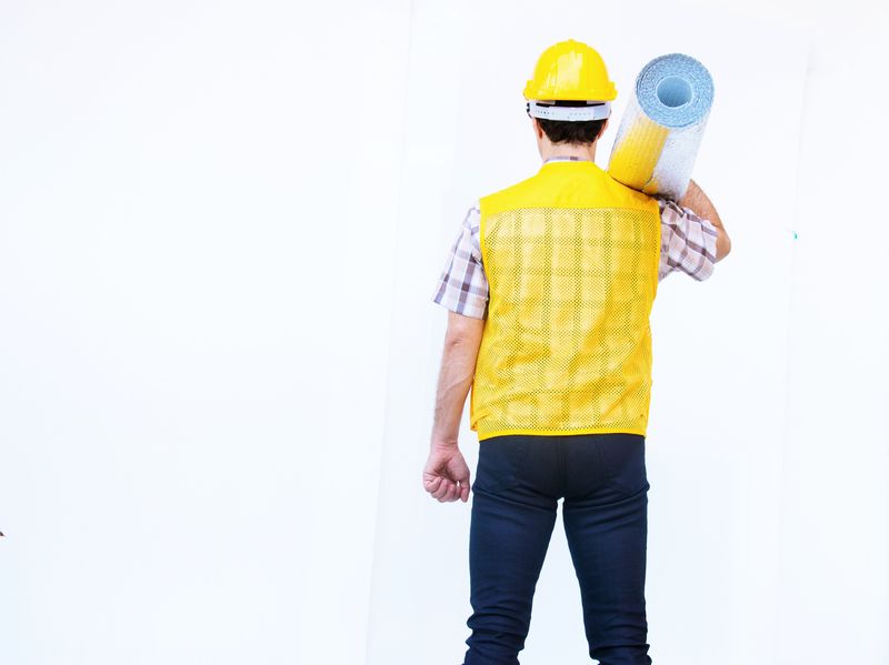微笑的建筑工人戴着黄色的安全帽，在白色的背景上戴着绝缘材料。