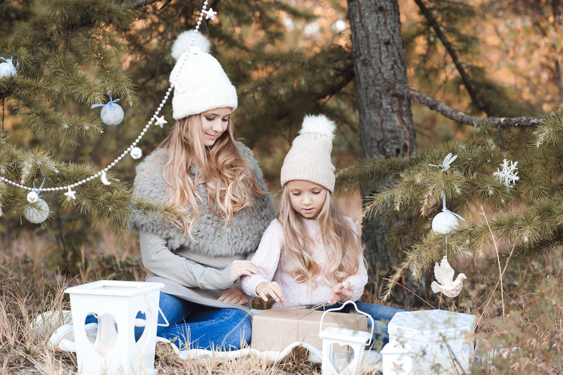 可爱时尚的女孩戴着针织帽子和毛衣在户外的圣诞树下打开圣诞礼物。假期。