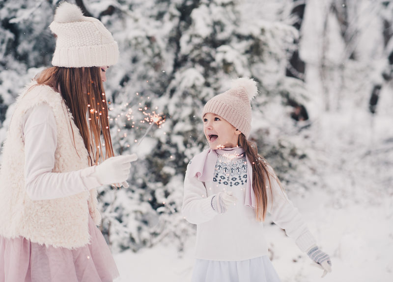 两个小女孩在户外的雪地里玩得很开心。玩火花。穿着针织冬装。团结。圣诞节庆祝。