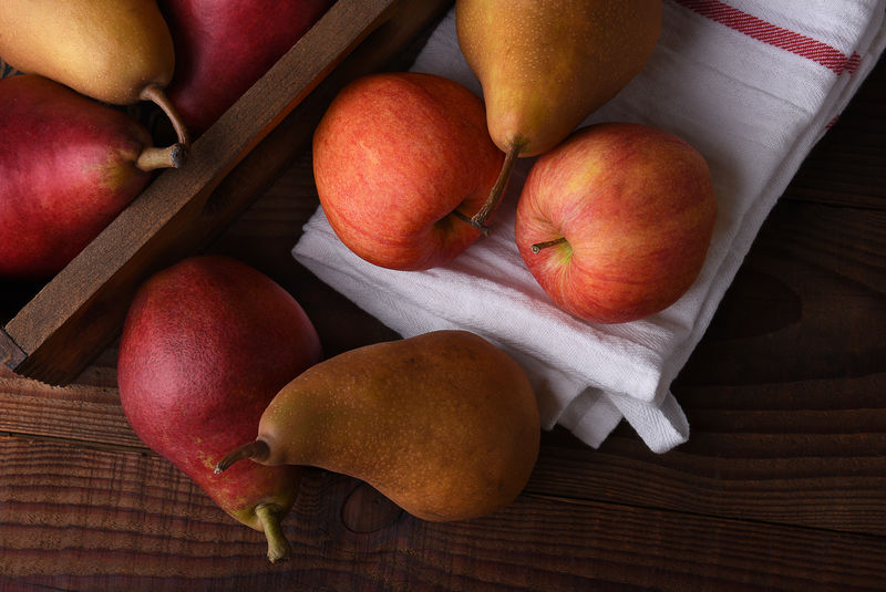 新鲜采摘的梨和苹果放在木箱里，毛巾放在乡村的木桌上。水平格式的俯视图。