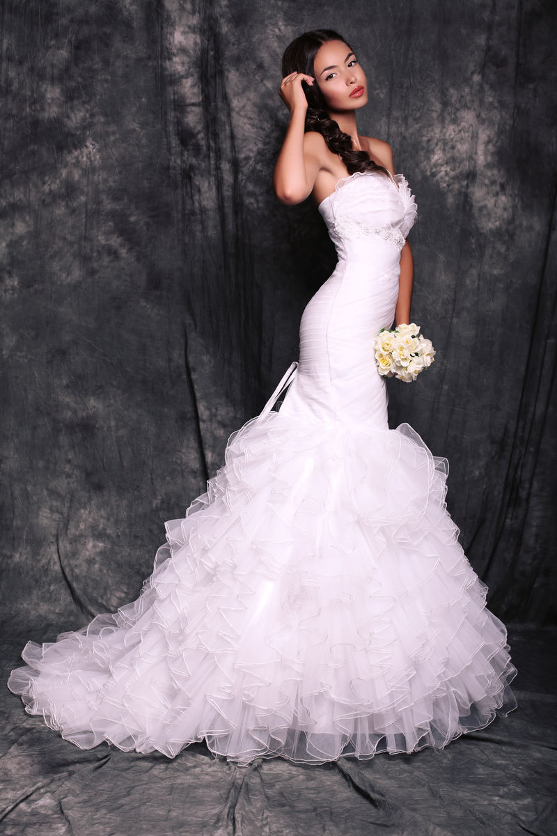 美丽的新娘穿着优雅的礼服摆着结婚花束
