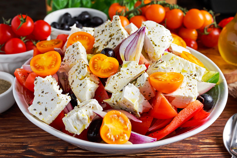 希腊色拉配新鲜甜椒、红洋葱、橙樱桃西红柿、黄瓜、黑橄榄和费塔奶酪，在木桌上淋上初榨橄榄油
