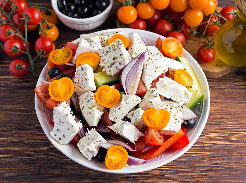 希腊色拉配新鲜甜椒、红洋葱、橙樱桃西红柿、黄瓜、黑橄榄和费塔奶酪，在木桌上淋上初榨橄榄油