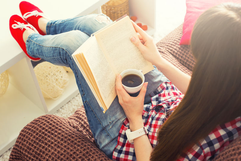 坐在沙发上拿着咖啡杯看书的女人