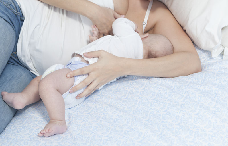 年幼的母亲用母乳喂养躺在卧室里的婴儿