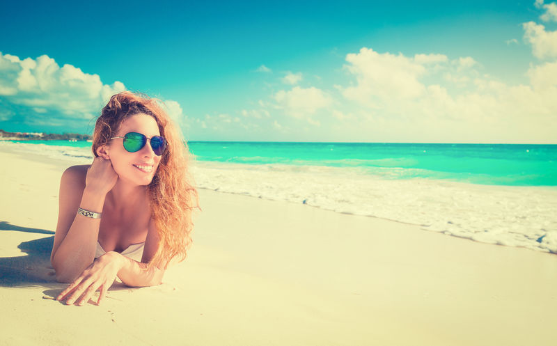 带着墨镜的微笑美女在海滩上晒太阳