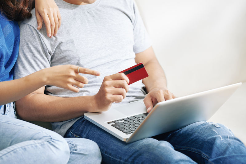 一对夫妇在使用笔记本电脑和信用卡购物时通过互联网购物的照片