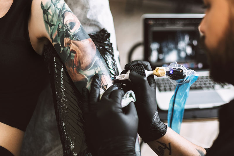 特写专业黑手套纹身大师在现代工作室用纹身机在女孩手上做纹身