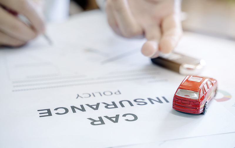 以红色汽车玩具和模糊人手形象的汽车保险单为保险单概念