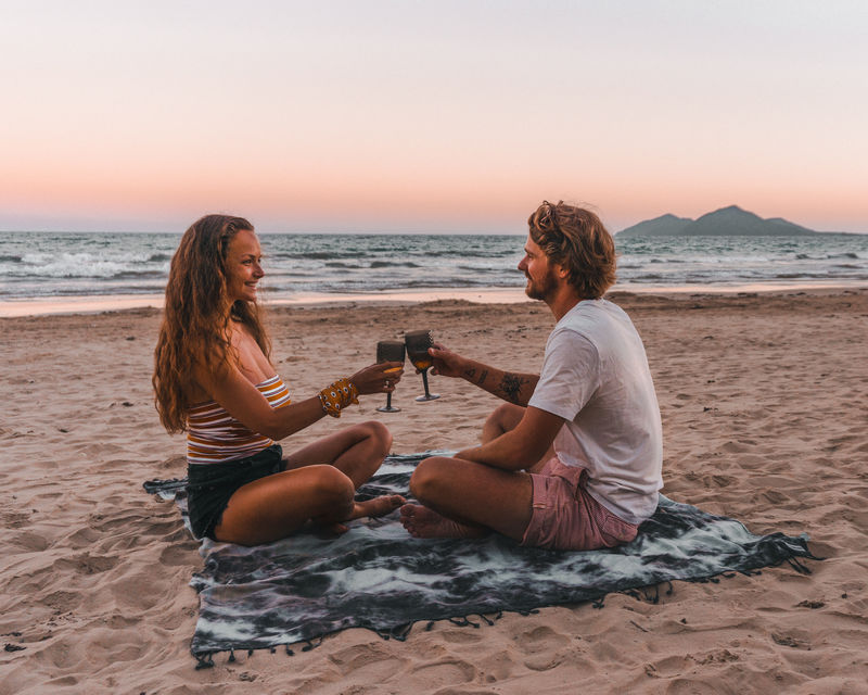 男人和女人坐在沙滩上烤酒杯