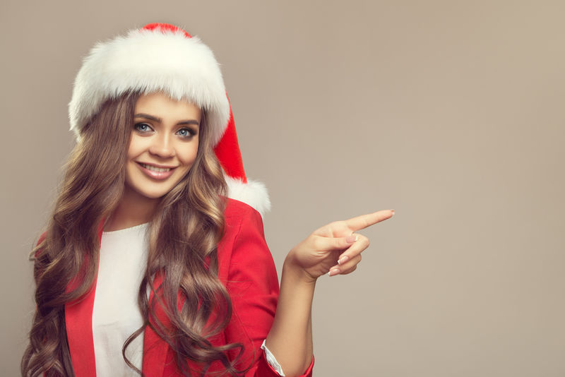 圣诞帽上可爱微笑的女人的肖像-用手指着复制空间-圣诞节