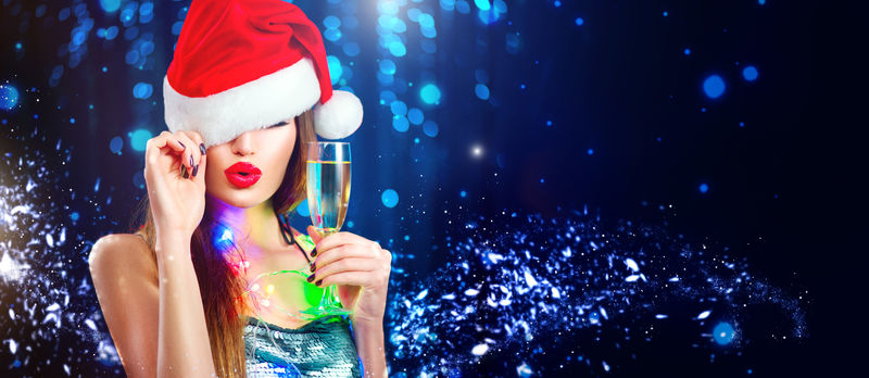 圣诞节性感女人-戴着圣诞老人红唇帽子的美女模特-手里拿着香槟酒杯在夜总会派对上庆祝-冬季宽背景的特写魅力肖像-带文案空间
