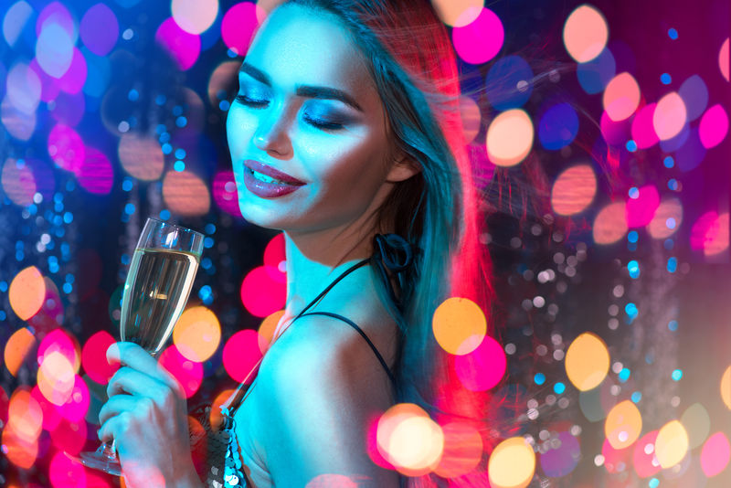 性感的模特女郎在迪斯科派对上拿着一杯香槟-在蓝色的背景下喝着香槟-拥有完美时尚妆容的美女-圣诞节和新年庆祝活动