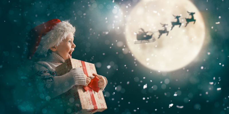 圣诞快乐！圣诞礼物可爱的小朋友-圣诞老人乘雪橇飞向月亮的天空-快乐的孩子享受假期-在黑暗背景下赠送礼物的女孩肖像