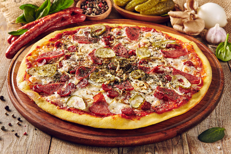 木桌上的肉和蔬菜披萨-香肠片和腌黄瓜的面团成分-意大利外卖菜-街头小吃-奶酪烤快餐