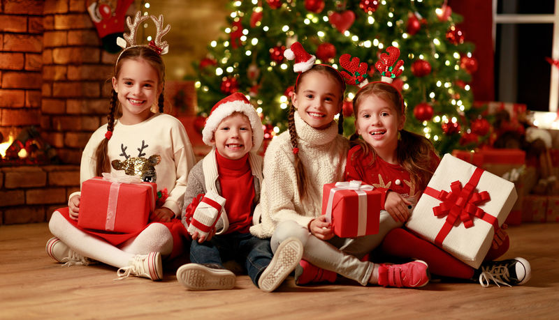 圣诞快乐！在圣诞树和壁炉旁的家里-带着礼物的快乐的孩子们