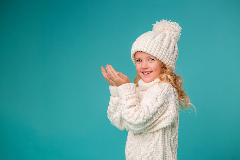 金发小女孩在白色冬季针织帽和蓝色背景隔离毛衣-空间文字-孩子们在冬天和雪中快乐-冬装