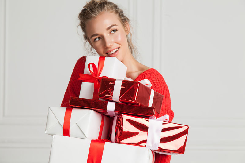 一个微笑着的漂亮女人的特写镜头，白色内里穿着节日的红色毛衣，手里拿着一堆礼物