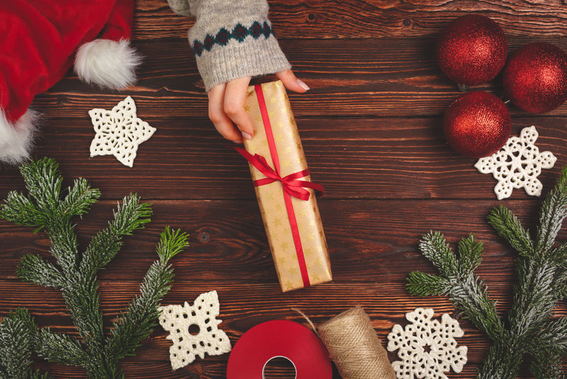 手拿毛衣，拿着礼物放在木制桌子上，上面有圣诞装饰品