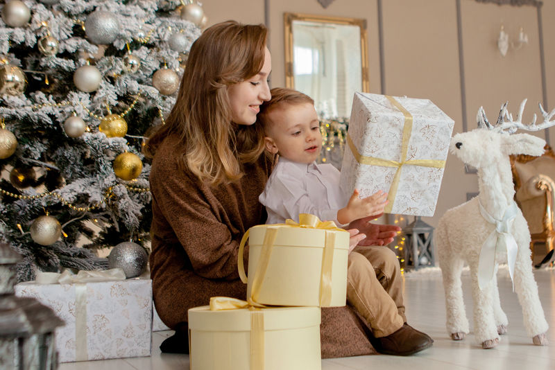 妈妈和她的小儿子在舒适的客厅里打开圣诞礼物。家庭度假时间