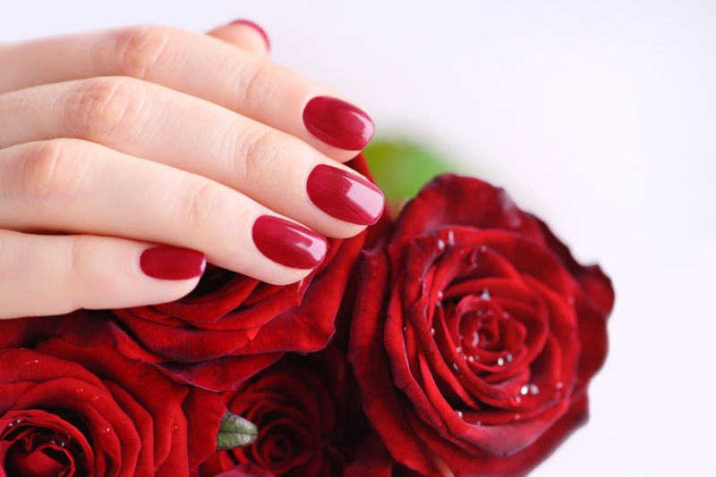 一个女人的手拿着红色的指甲和一束红玫瑰。