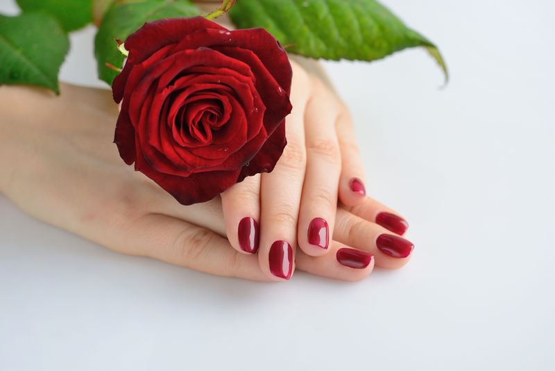 一个女人的手，深红色的指甲，白b上有红玫瑰