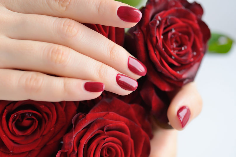 手上有红色指甲和一束红玫瑰的女人