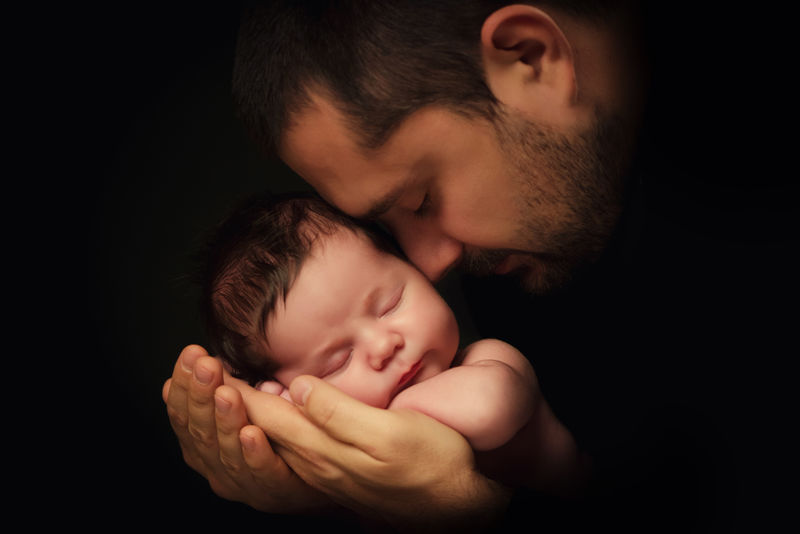 爸爸抱着他刚出生的孩子。父爱。黑色背景上的特写肖像
